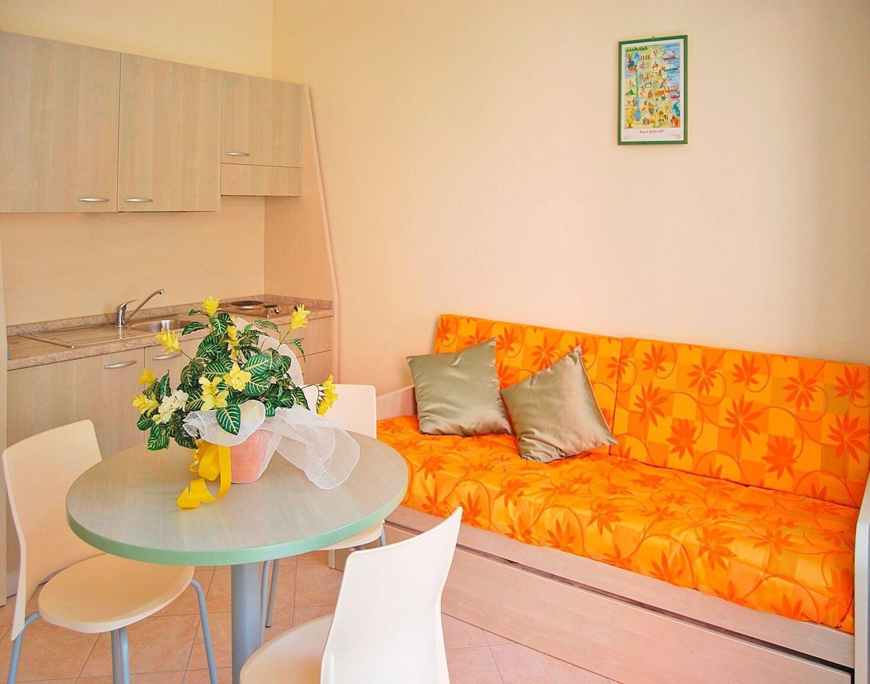 A compact living space with a kitchenette, a round dining table with chairs, and an orange sofa with cushions.