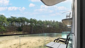 A balcony with a glass railing overlooking a forested area and a sandy beach. - Comfortable Apartment in Egmond aan Zee Near Sea (Egmond aan Zee)