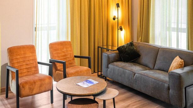 A modern living room with a grey sofa, two orange armchairs, a round coffee table, and a small side table. - Comfortable Apartment in Egmond aan Zee Near Sea (Egmond aan Zee)