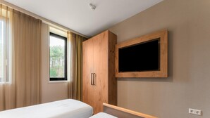 A bedroom with two beds, a wooden wardrobe, a mounted TV, and a window with curtains. - Comfortable Apartment in Egmond aan Zee Near Sea (Egmond aan Zee)