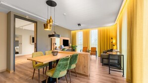 A modern hotel room with a wooden dining table, green patterned chairs, a kitchen area, and a large window with yellow curtains. - Comfortable Apartment in Egmond aan Zee Near Sea (Egmond aan Zee)