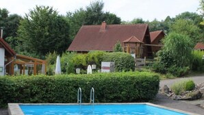 Ein Swimmingpool mit drei aufblasbaren Ringen, umgeben von einer Hecke und einem Gebäude mit rotem Dach.