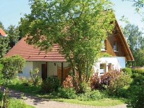 A two-story house with a red-tiled roof, surrounded by lush greenery and trees.