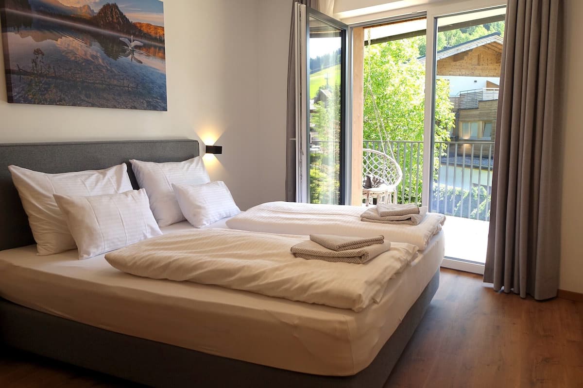 Ein Schlafzimmer mit einem großen Bett, einer Kopfteil und Blick auf einen Balkon mit einem Sessel.