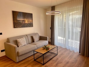 Una sala de estar moderna con un sofá, una mesa de centro, un cuadro y un ventanal con cortinas.