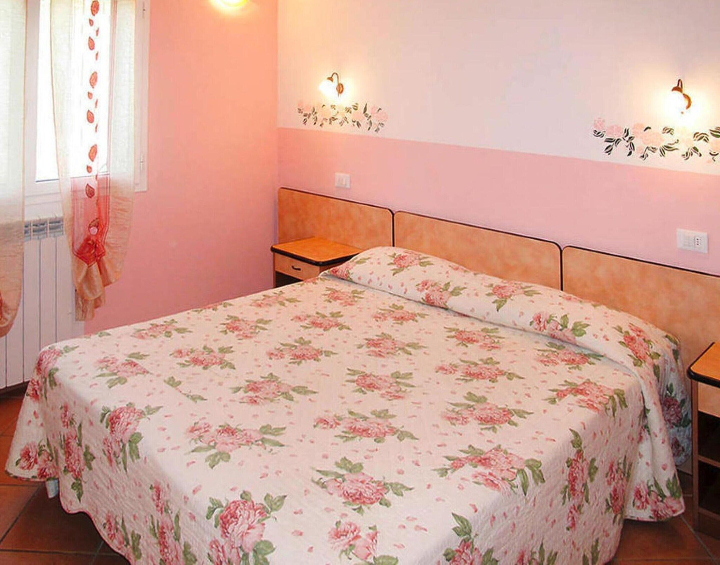 A bedroom with a floral bedspread, wooden headboard, two bedside tables, and wall-mounted lights.