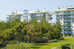 Ett modernt hotell med flera våningar och balkonger, omgivet av grönområden.
