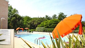 A swimming pool with a person on a pink float, surrounded by orange umbrellas, and a sign indicating the pool's features. - Holiday Resort Parco e Acacie, Bibione Pineda (San Michele al Tagliamento)