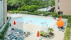 A rooftop pool with lounge chairs and umbrellas, surrounded by greenery and a building.
