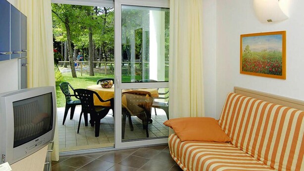 A living area with a sofa, a television, a dining table with chairs, and a sliding glass door leading to an outdoor space.