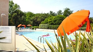 A swimming pool with a person on a pink float, surrounded by orange umbrellas, and a sign indicating the pool's features. - Holiday Resort Parco e Acacie, Bibione Pineda (San Michele al Tagliamento)