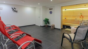 Un área de espera con sillas rojas, un mostrador de recepción de madera, un reloj y una planta en la pared.