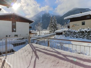 Schneebedeckte Berglandschaft mit Gebäuden, darunter ein Hotel namens "Alpen Sonne", und ein Metallgeländer im Vordergrund.