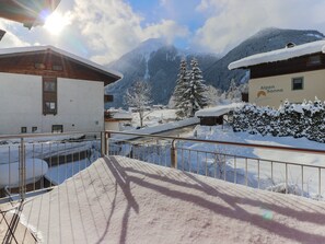 Lumipeitteinen vuoristomaisema, jossa on rakennuksia, mukaan lukien hotelli nimeltä ’Alpen Sonne’, ja etualalla näkyy metallinen kaide.
