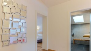 Habitación de hotel con piso de madera, un espejo decorativo montado en la pared, una cama y un baño con banco y lavamanos.
