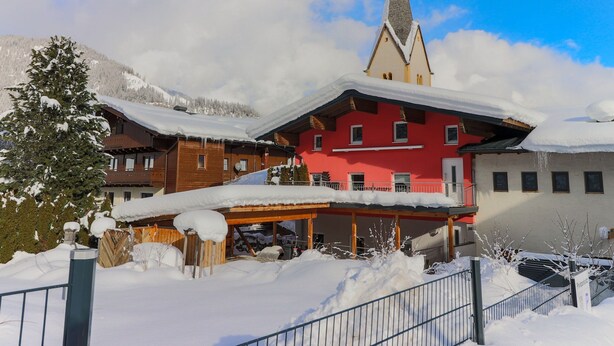 Un edificio rojo con techo pronunciado, rodeado de árboles y montañas cubiertas de nieve.
