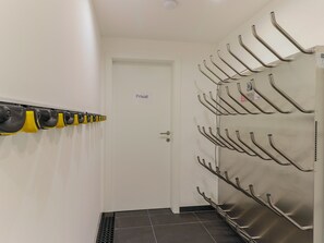 Een gang met een 'Privat' deur, een kapstok met geel en zwart materiaal, en een metalen rek met haken.