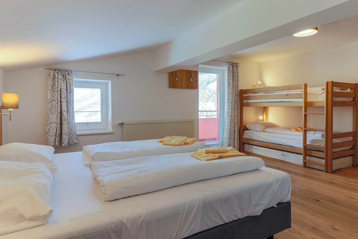 A room with two beds, a bunk bed, a window, a radiator, and a lamp.