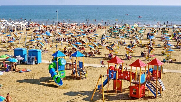 Una playa concurrida, con muchas sombrillas y gente.