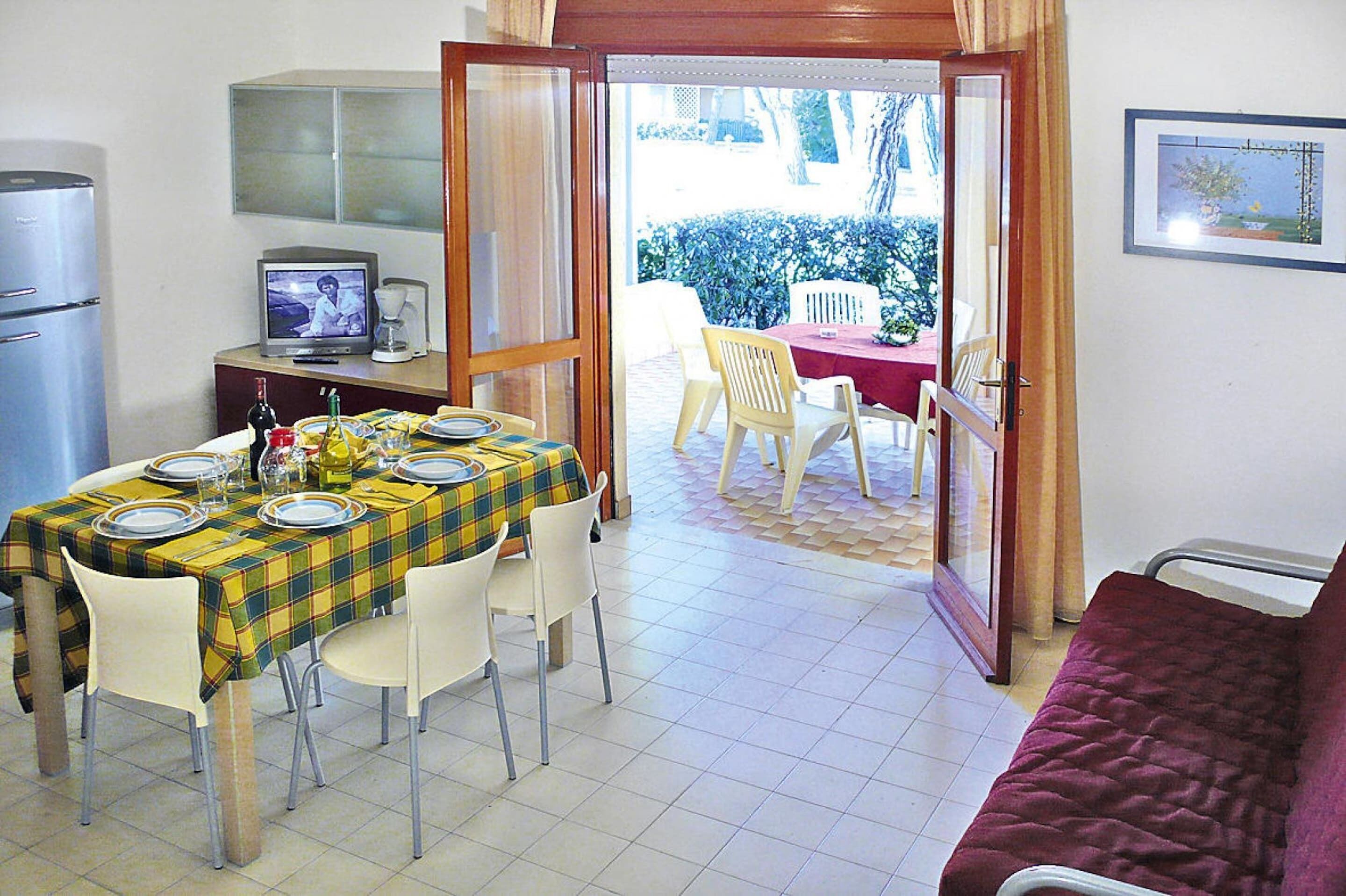A dining area with a table set for four, a television, and a refrigerator.