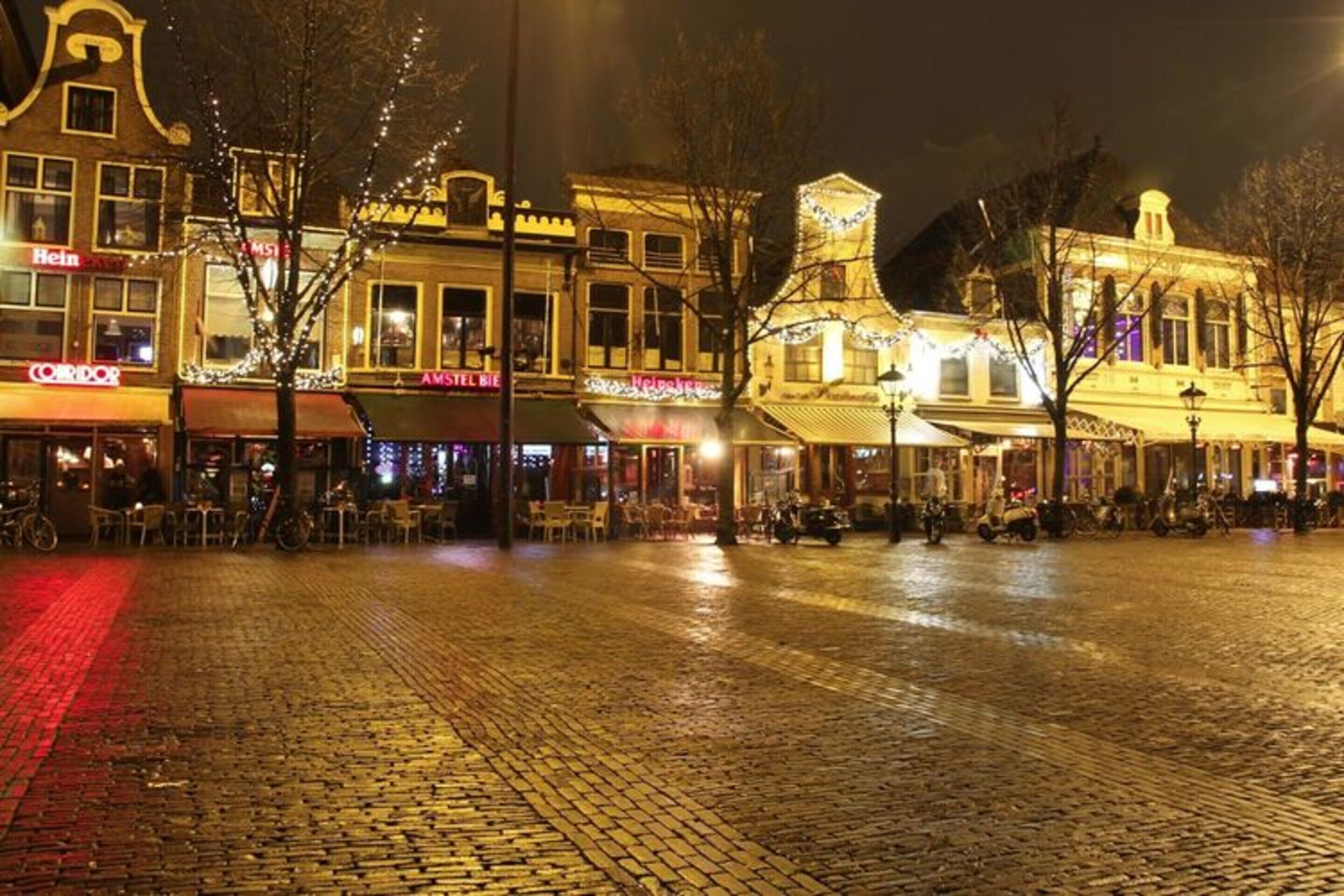 A cobblestone square with historic buildings, outdoor seating, and illuminated storefronts.