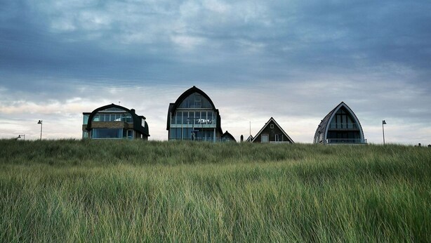 Three modern houses with large windows and unique architectural designs, situated on a grassy hill under a cloudy sky. - Luxury Apartment in a Residence Right on the Boulevard and the Beach (Egmond aan Zee)