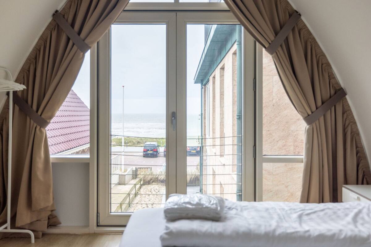 Un dormitorio con cama, ventana y cortinas.