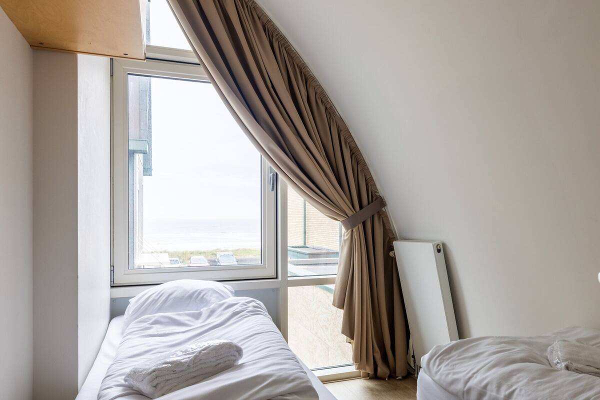 Habitación de hotel con dos camas, un ventanal con cortinas y vistas al mar.
