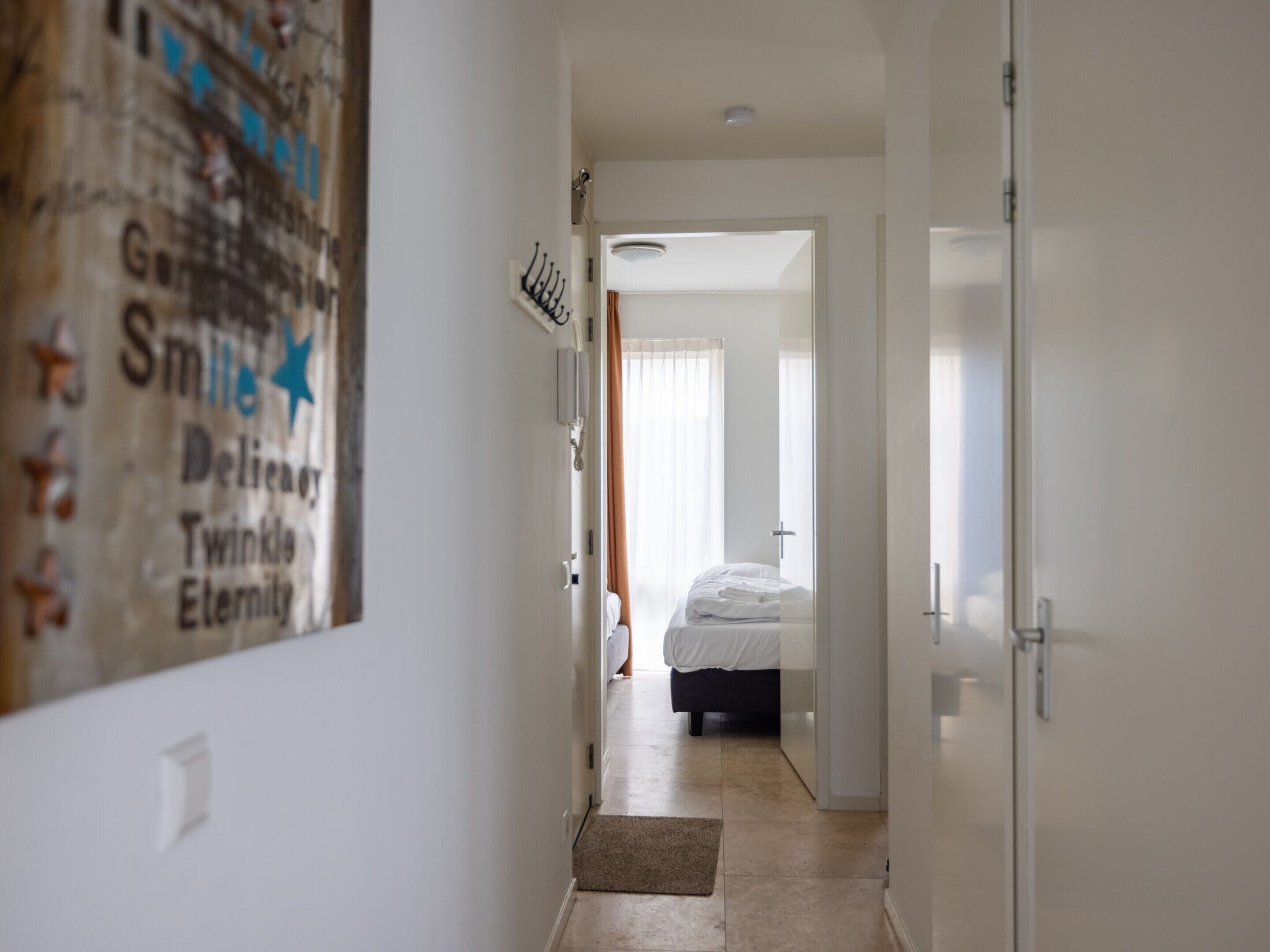 A hallway leading to a bedroom with a bed, a door, and a wall-mounted telephone.
