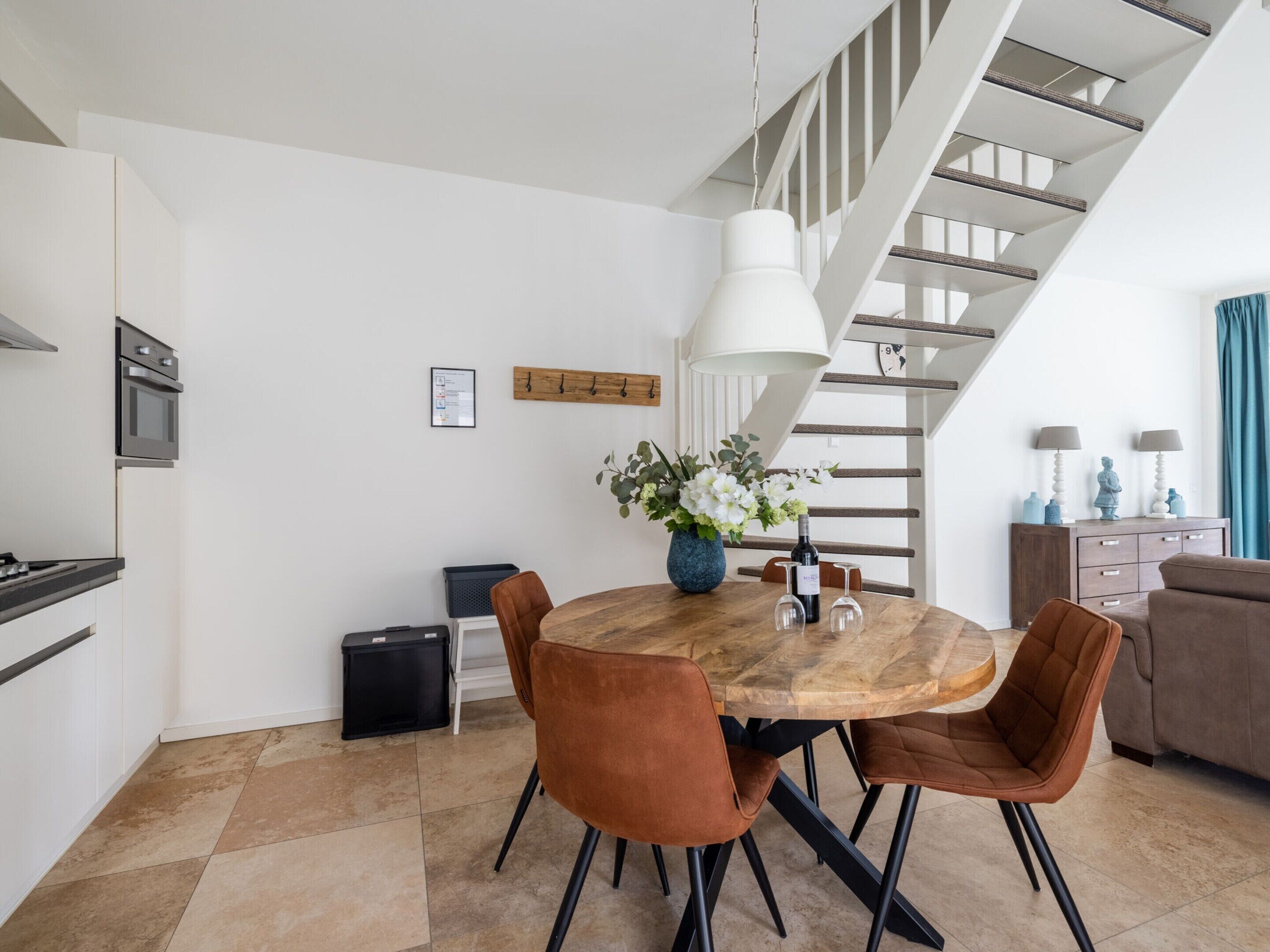 A modern kitchen with a dining area, featuring a wooden table, brown chairs, and a hanging light fixture.