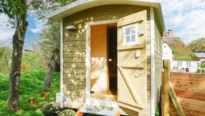 Een klein houten huisje met een geopende deur, een raam en een houten terras.