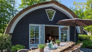 Un espacio comedor al aire libre acogedor, con mesa de madera y sillas de mimbre, rodeado de abundante vegetación.