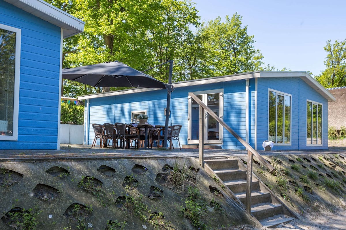A blue house with a dining area, outdoor seating, and a staircase leading to a deck.