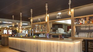 Zona de bar con mostrador de madera, varias lámparas y una variedad de botellas y vasos.