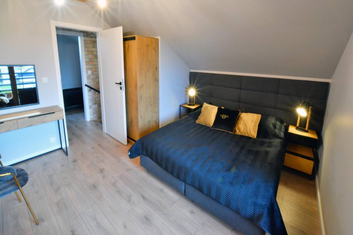 A bedroom with a bed, bedside tables, a desk, and a TV.