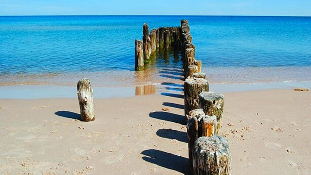 Una playa arenosa con un camino de madera que lleva al agua.