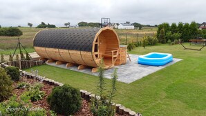 A cylindrical wooden structure with a black roof, a wooden deck, and a blue inflatable pool in a grassy yard. - Holiday House, Sauna, Whirlpool, Mielenko (Mielno)