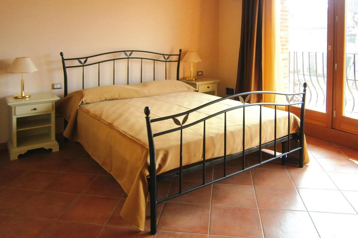 Un lit avec un cadre en métal, une table de chevet avec une lampe et une fenêtre avec des rideaux.