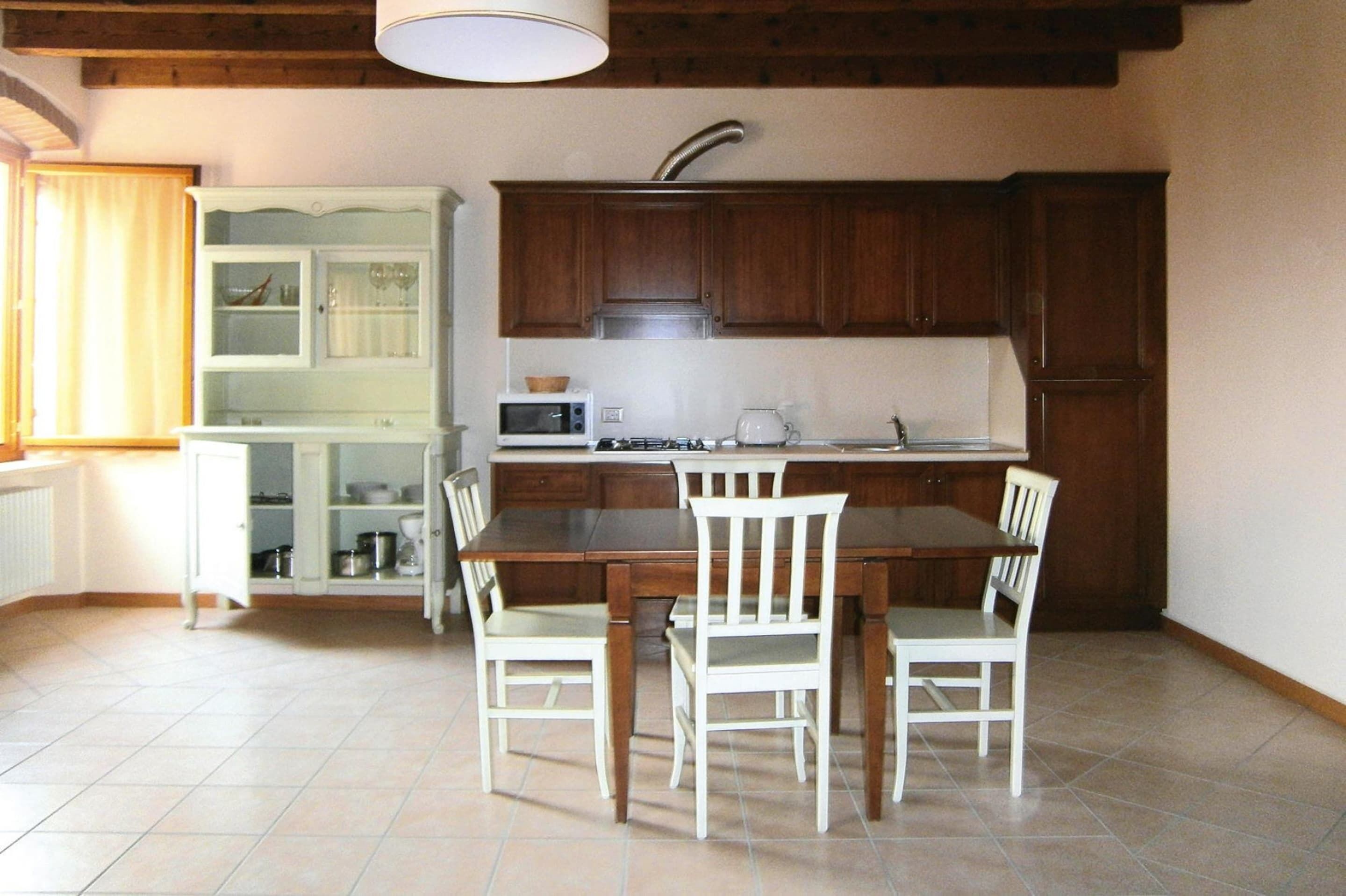 Una cucina compatta con mobili in legno, un tavolo da pranzo con quattro sedie, un forno a microonde e un bollitore.
