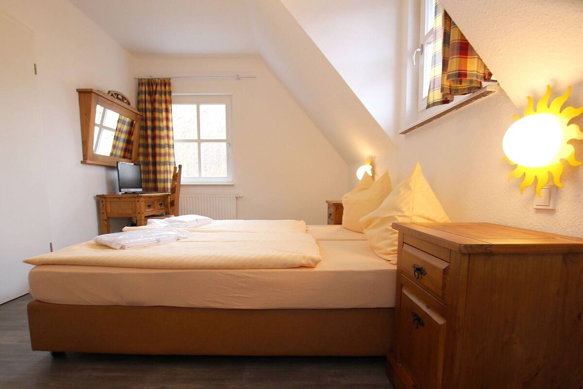 A bedroom with a bed, a wooden dresser, a nightstand, a television, and a window with curtains.