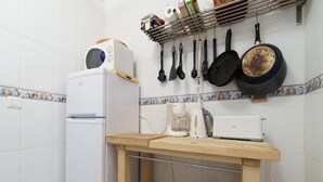 Eine kleine Küche mit weißen Fliesen, einem weißen Kühlschrank, einer Kaffeemaschine, einem Toaster und einem Holzboden mit Küchenutensilien.
