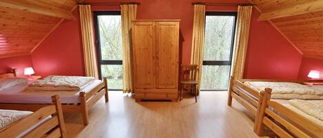 A room with wooden floors, two beds, a wardrobe, and large windows.