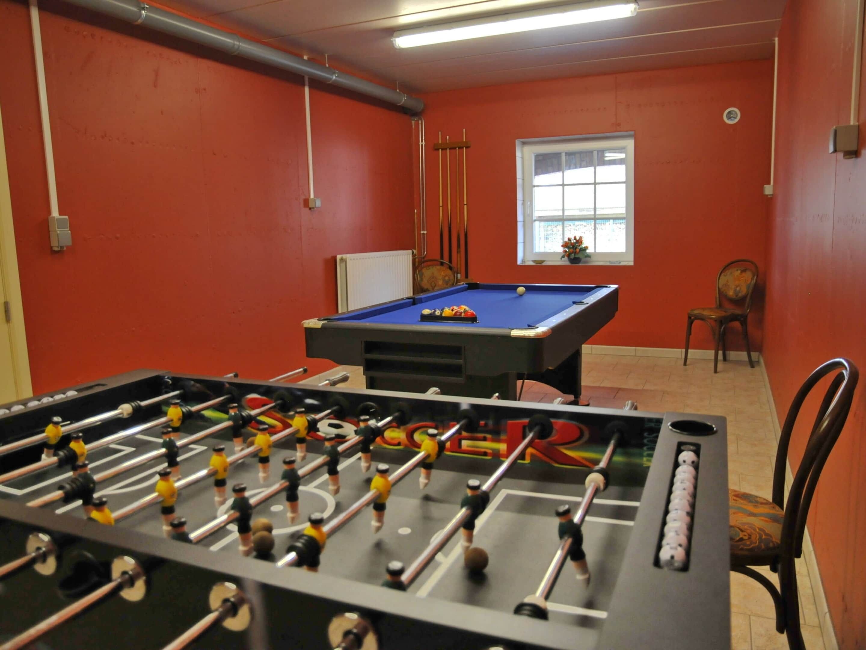 A room with a foosball table, a pool table, and a window with a view.