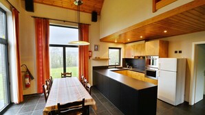 A modern kitchen with a central island, wooden ceiling, and large windows. - Modern Holiday Home in Somme-leuze With Garden (Somme-Leuze)