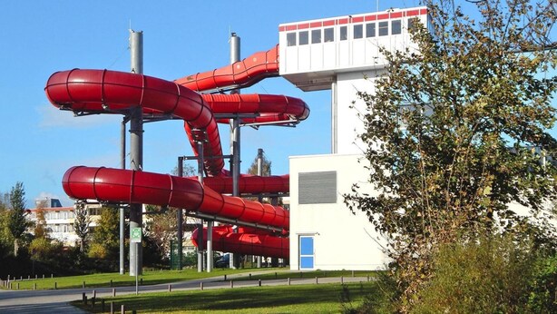 A building with a white exterior and a red water slide structure attached to it. - Doppelhaushalften im Ferienpark Weissenhauser Strand (Wangels)
