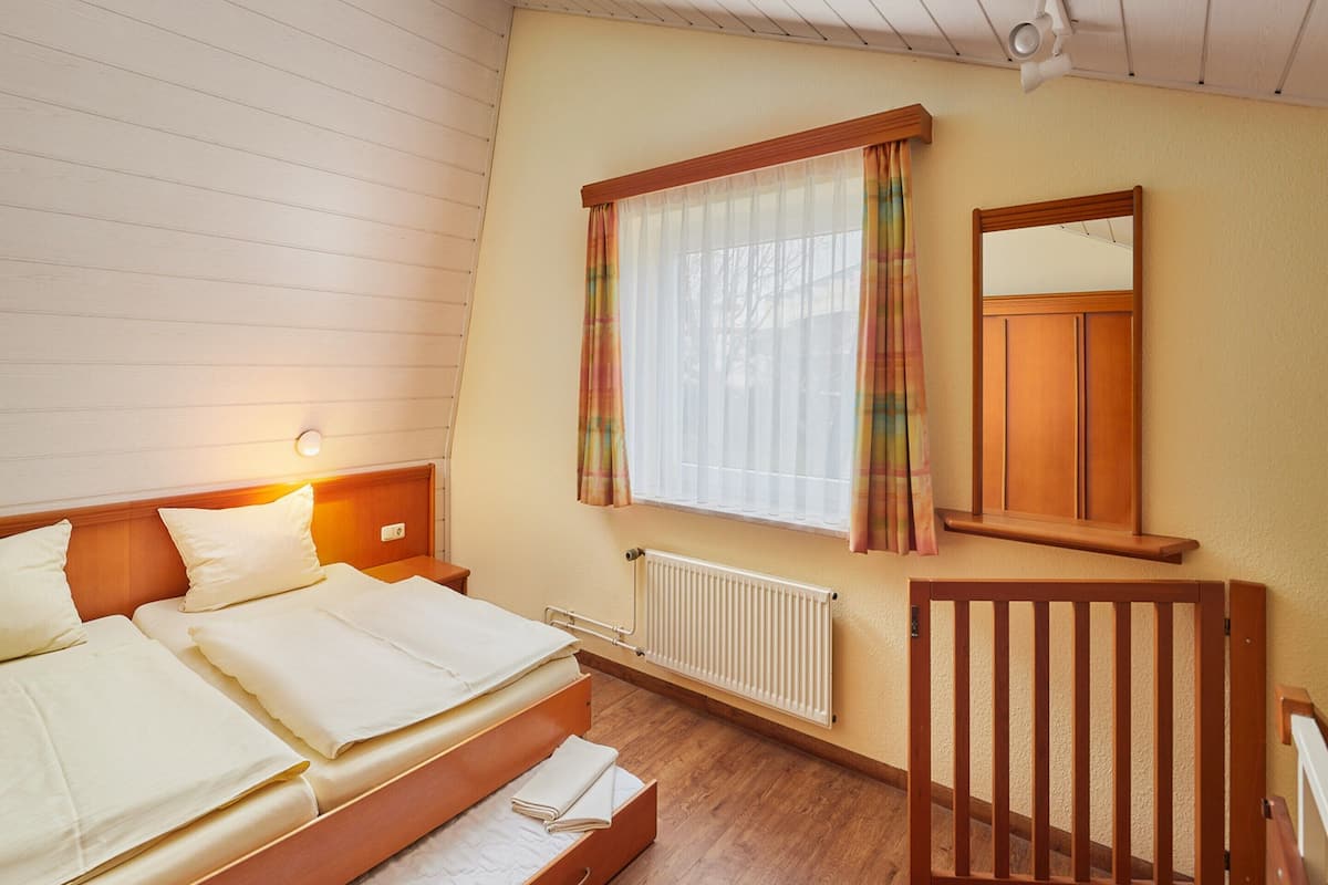 Et soveværelse med seng, natbord, vindue med gardiner, radiator og en træstol.