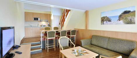 A compact living space with a kitchenette, a sofa, a dining area with chairs, and a television.