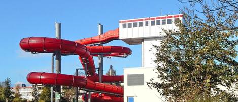 A water park with multiple red slides and a white building with a red roof.