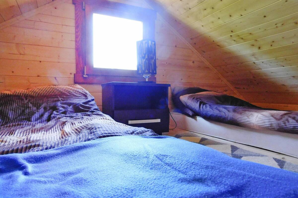 Ein kleines, gemütliches Schlafzimmer im Dachgeschoss mit geneigter Decke, einem Fenster und einem Bett mit einer gestreiften Decke.