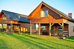Two wooden cabins with pitched roofs, each featuring a porch with seating and a window. - Holiday Homes for 7 People in Swinoujscie (Swinoujscie)
